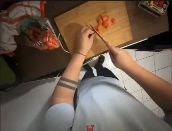 Vista desde la cabeza: dos manos picando verduras con cuchillo sobre una tabla